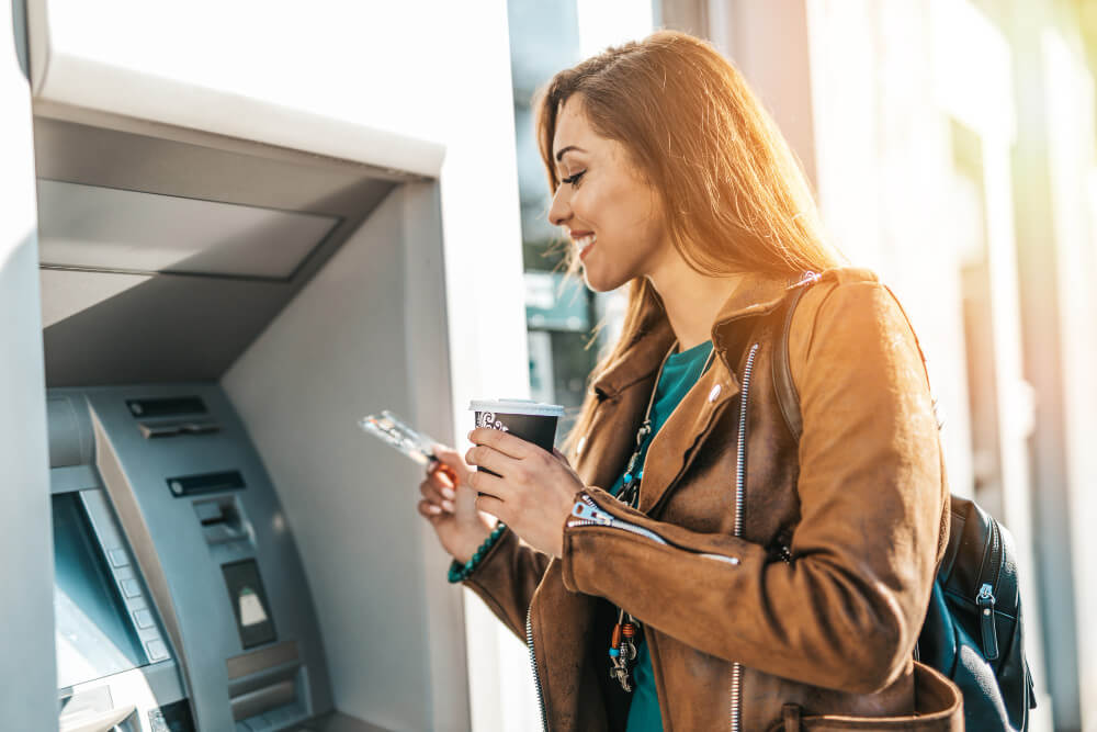 A woman standing in front of an ATM holding a credit card